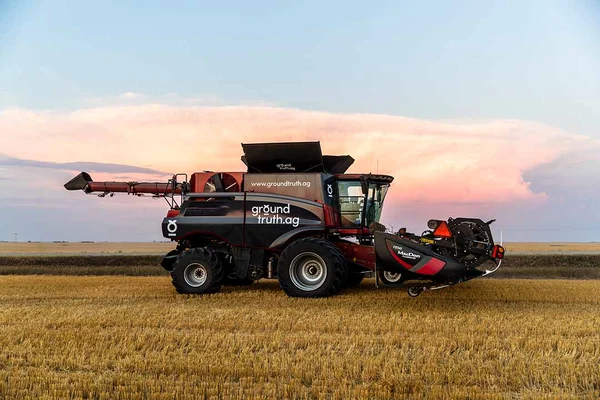A Ground Truth.ag branded red combine harvester working a wheat field at dusk under a dramatic pink and blue sky.