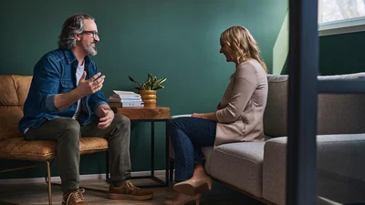 Two people engaged in conversation while seated across from each other in a modern lounge area with teal walls.