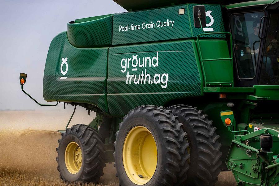 Close-up of a large Ground Truth Ag combine. The focus is on the side of the machine, highlighting its large yellow wheels and the green brand wrapped body.