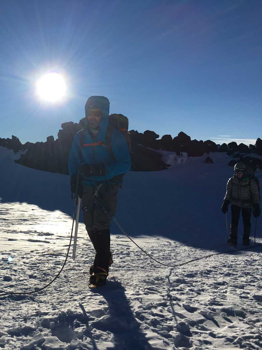 Two mountaineers roped together trekking across a snow-covered glacier under a bright sun.