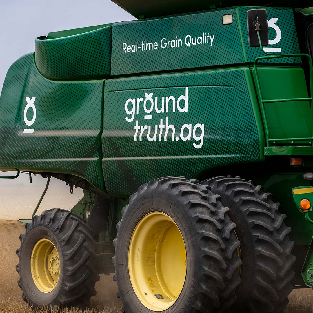 Close-up of a large Ground Truth Ag combine. The focus is on the side of the machine, highlighting its large yellow wheels and the green brand wrapped body.